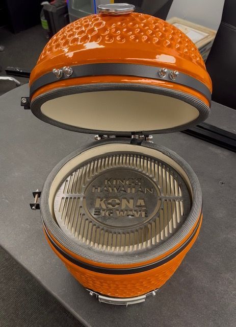 Opened orange ceramic Kamado grill, inside visible cooking grate and firebox.