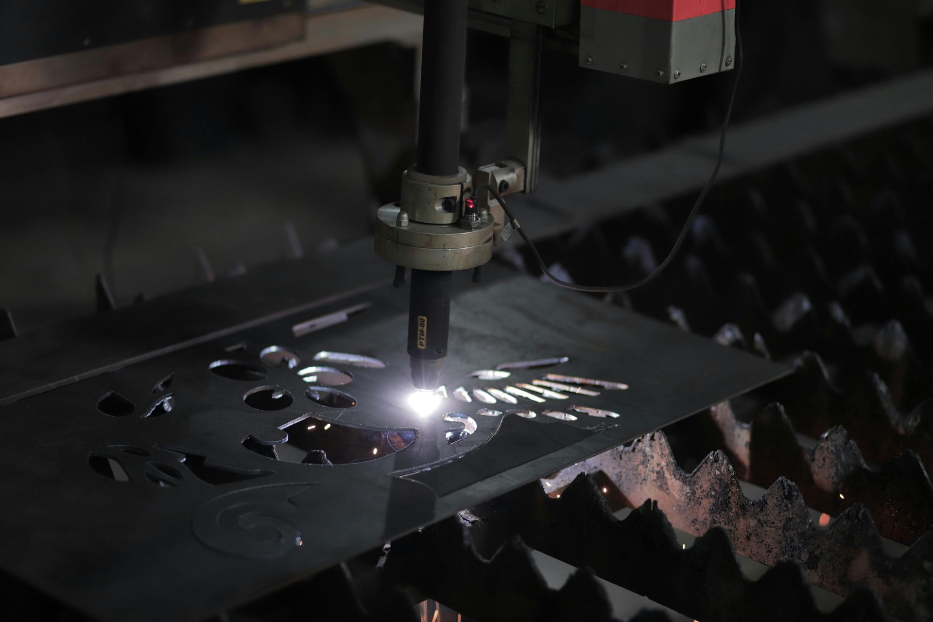A laser cutter precisely cuts a metal sheet, sparks flying, in an industrial setting.