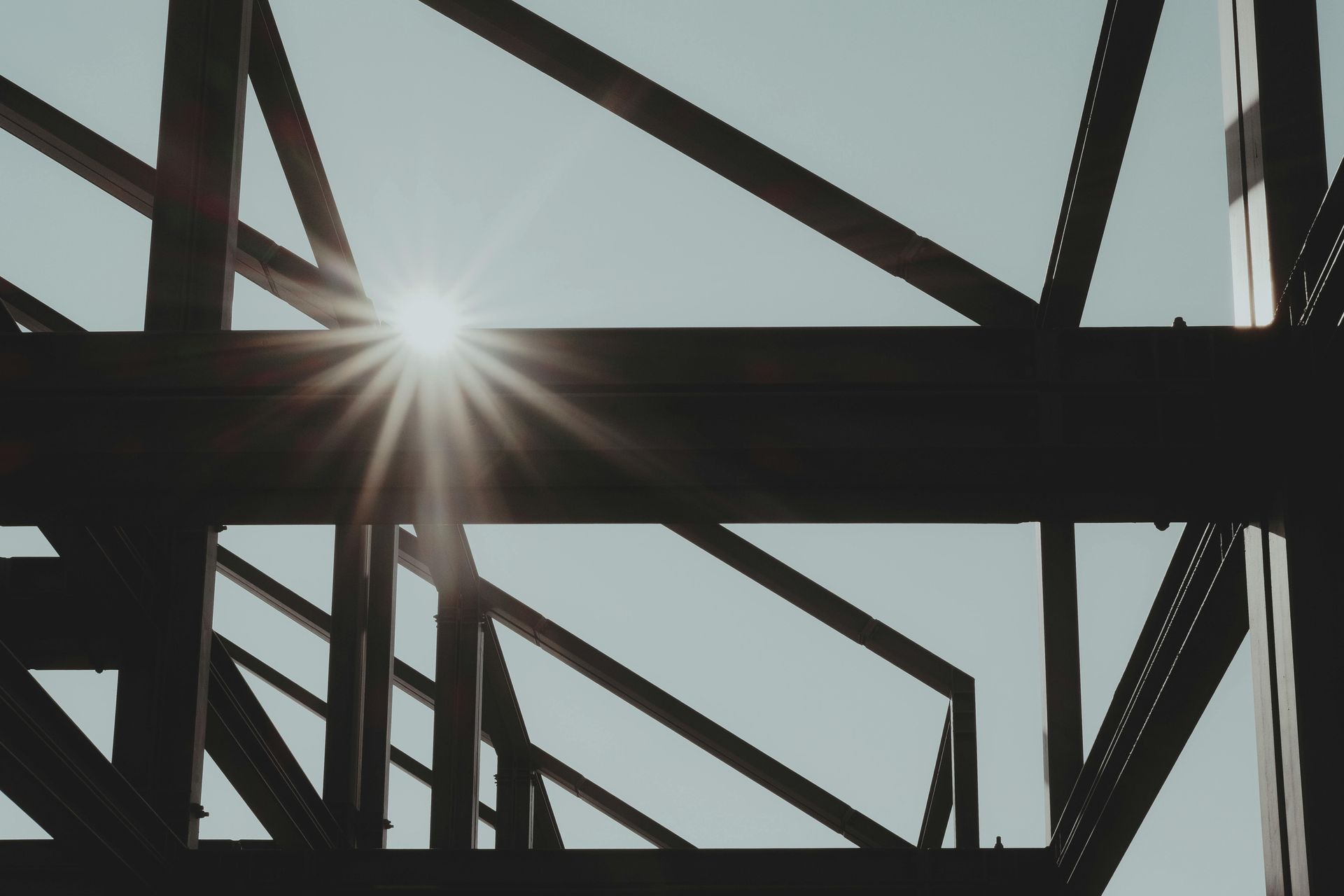 Sun shining through steel beams against a pale blue sky.