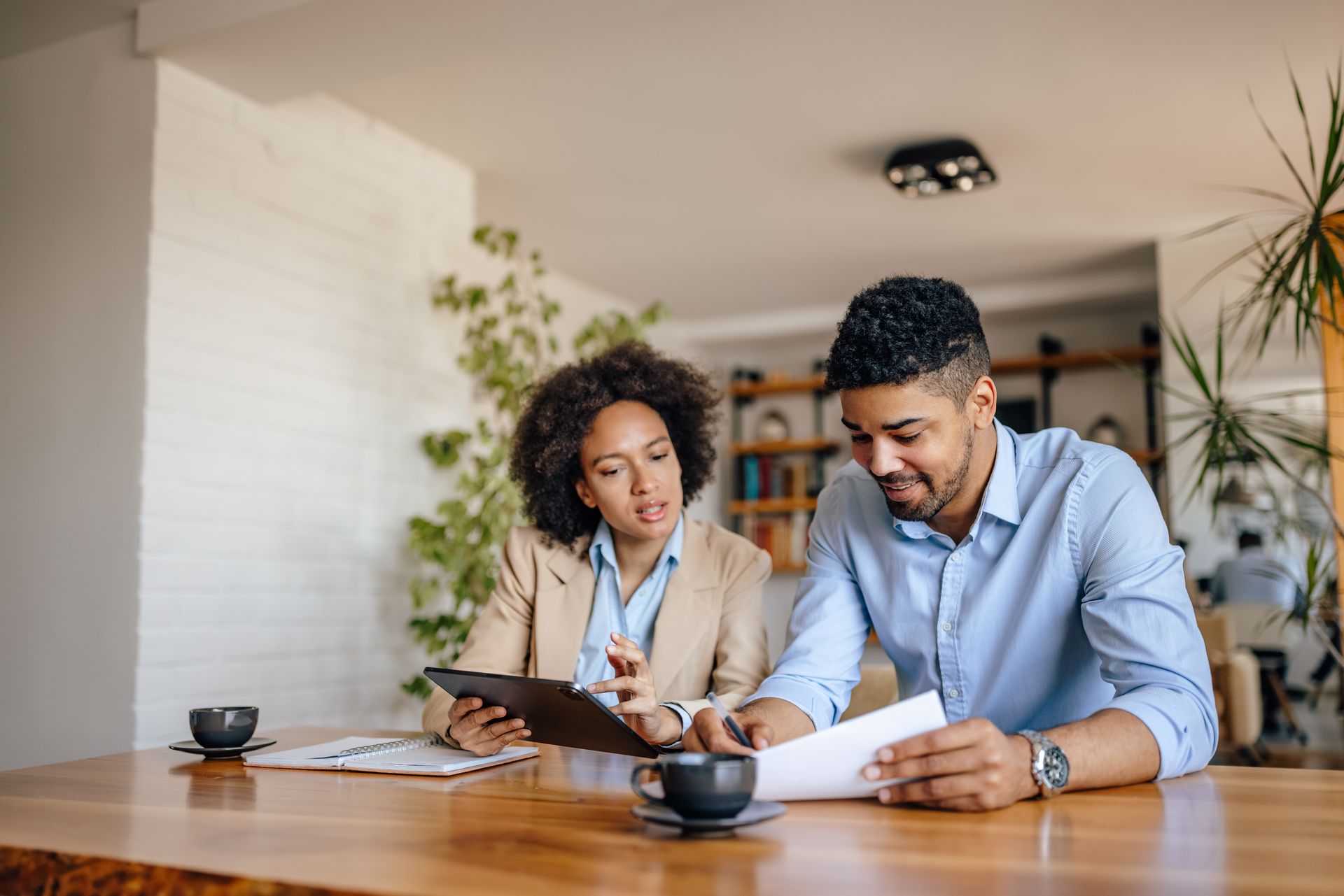 Two people reviewing documents at a wooden table in a bright home office