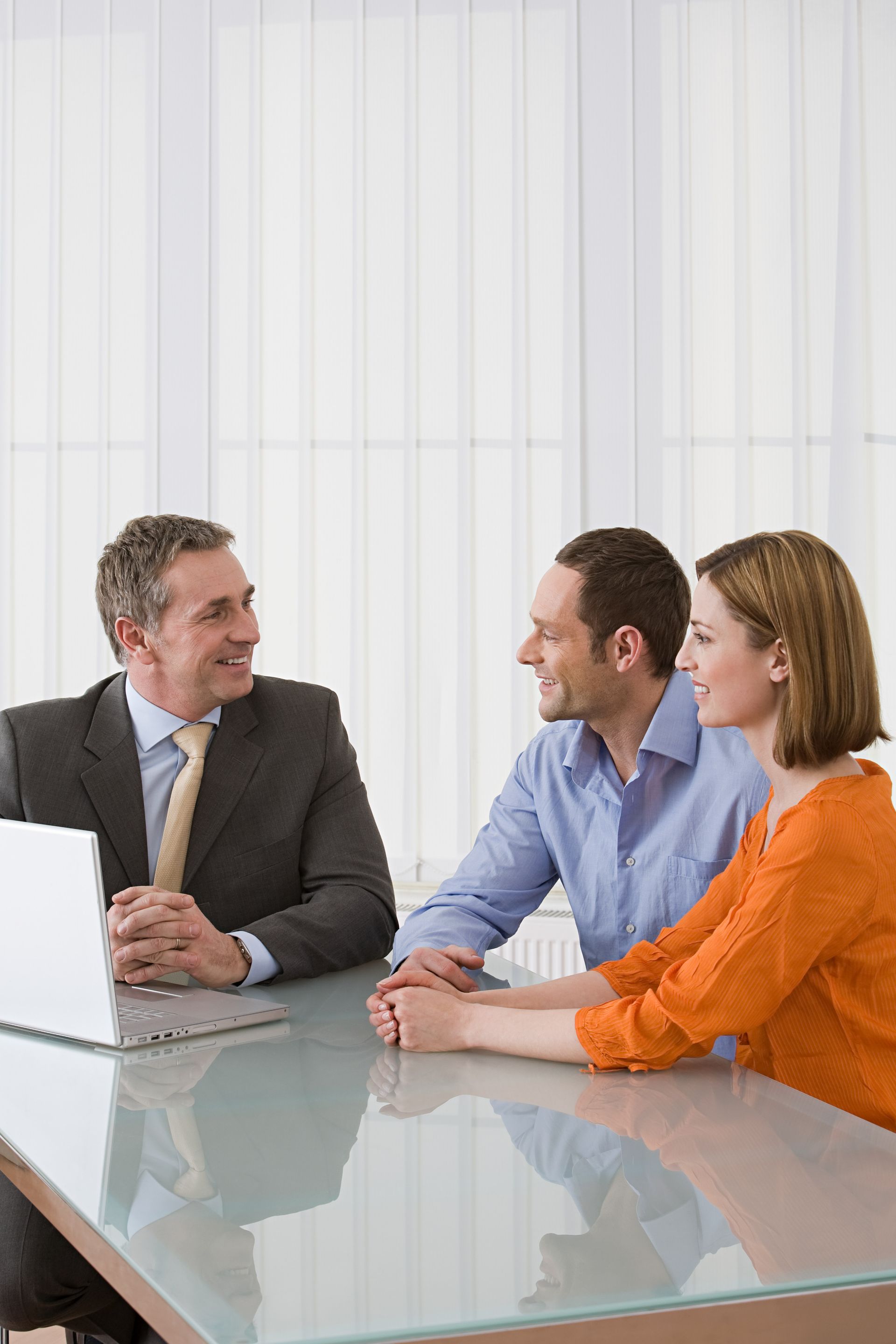 Three coworkers in a meeting at a glass table, discussing beside a laptop.