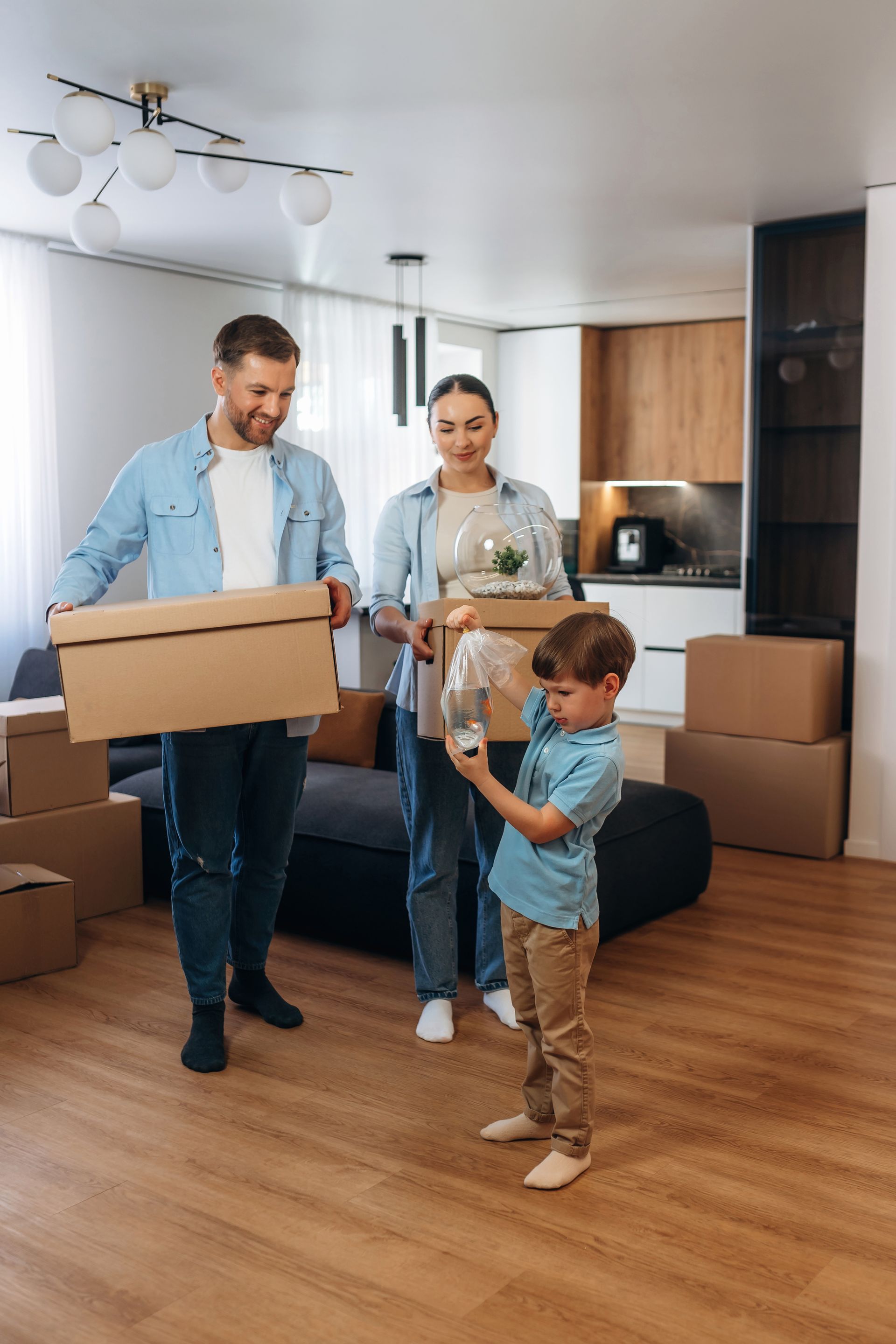 Family carrying moving boxes in a bright kitchen and living room.