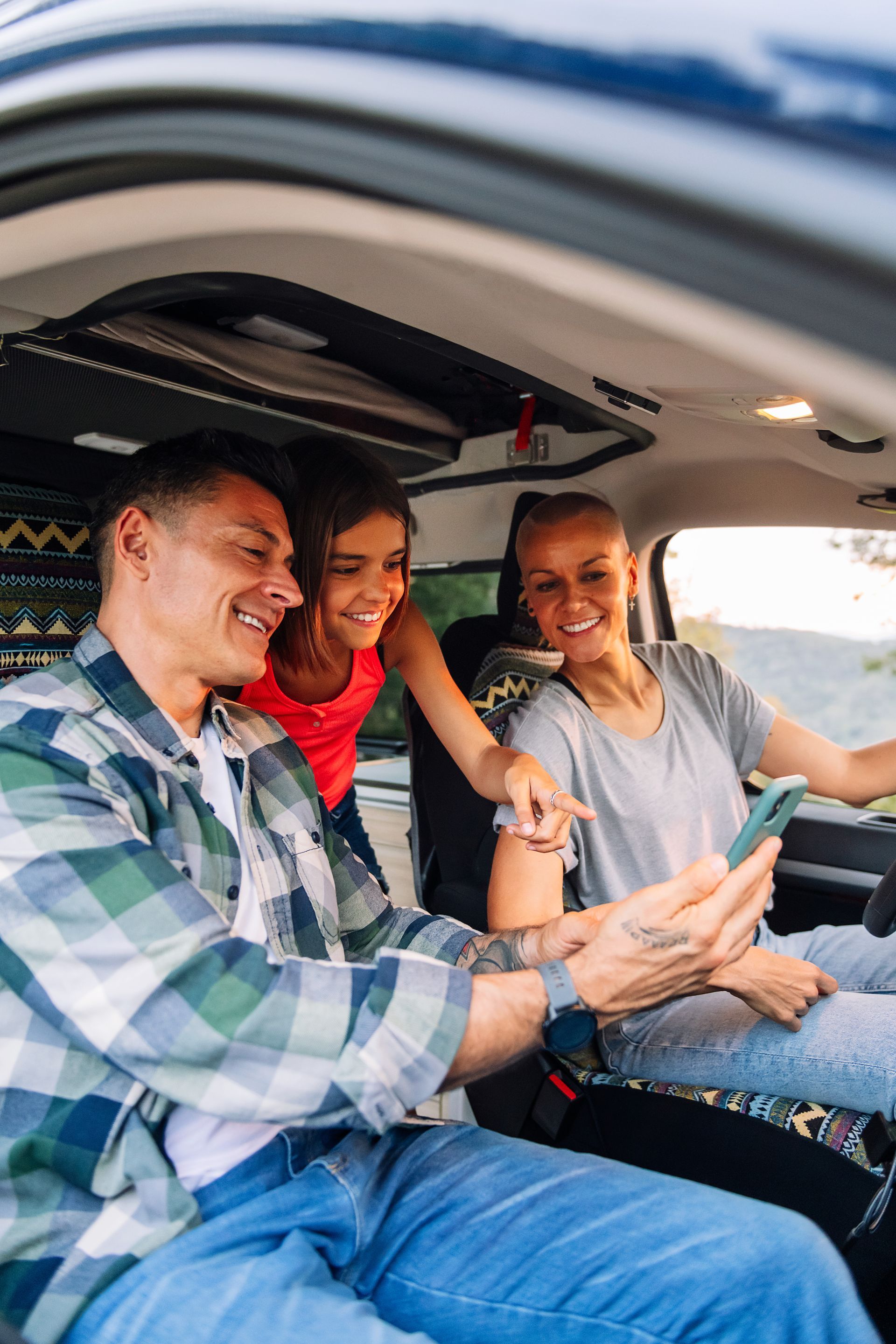 Man in plaid shirt smiles at child from car window.