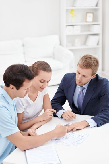 Four people in business attire reviewing documents around a white table in a bright office