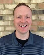 Smiling man in a navy striped polo standing against a brick wall.