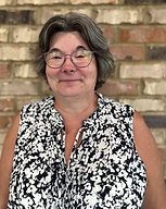 Smiling person in glasses wearing a black-and-white patterned sleeveless blouse against a brick wall