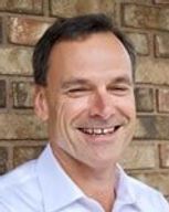 Smiling man in a light blue shirt standing against a brick wall