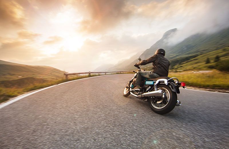 Motorcyclist riding on a winding mountain road under cloudy skies