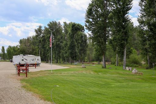 A rv parked in a grassy area with trees and a flag.