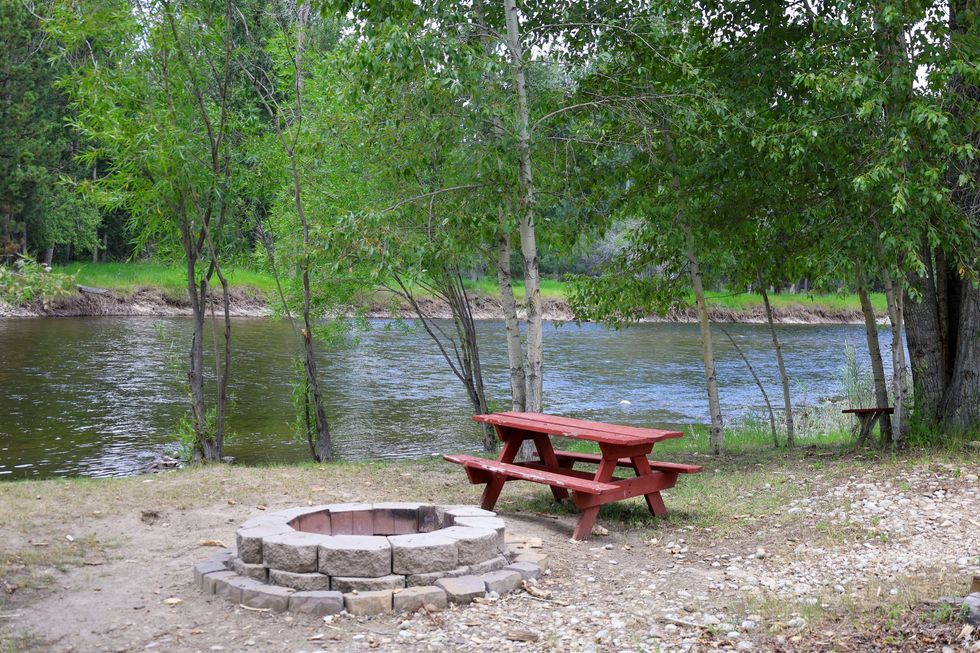 A picnic table is sitting next to a fire pit by a river.