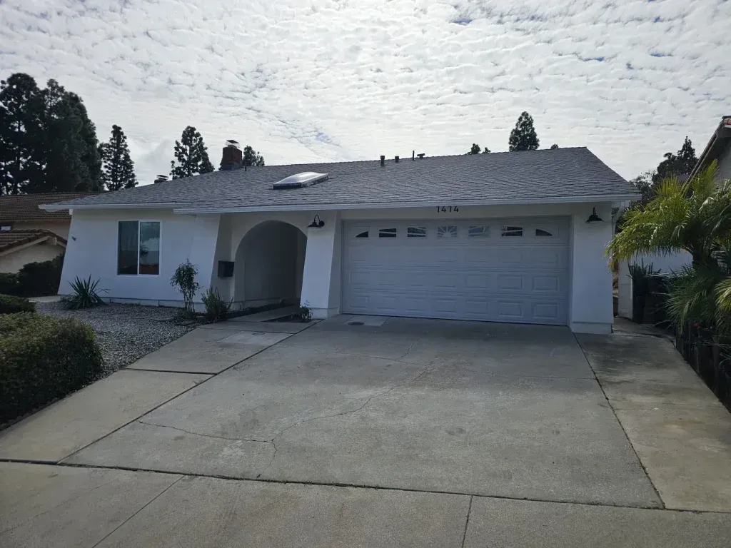 Single-story suburban house with a two-car garage and large concrete driveway under a cloudy sky