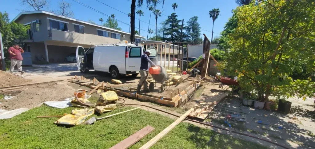 Workers building a wooden deck in a sunny yard beside a white van and house.