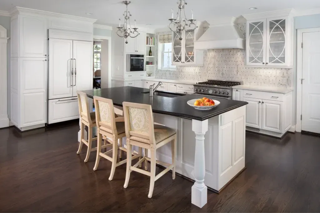 Bright white kitchen with island, wooden bar stools, chandeliers, and dark hardwood floors