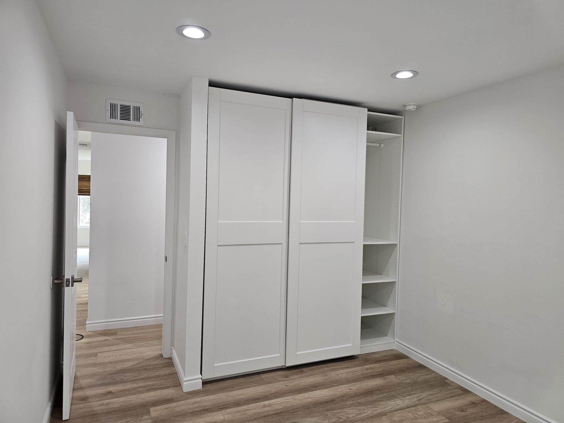 Bright empty room with white built-in closet, open shelving, and wood flooring