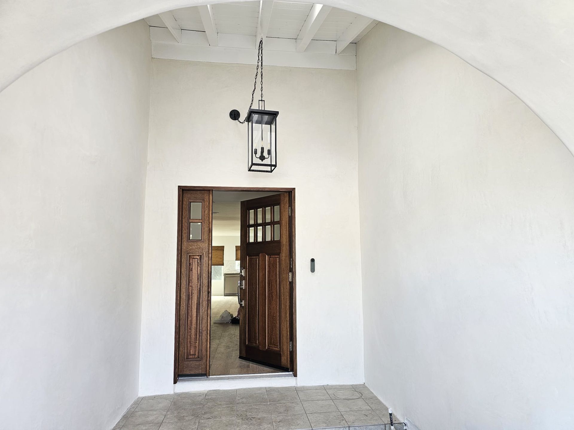 White arched hallway with open wooden doors and a hanging lantern light above the entrance