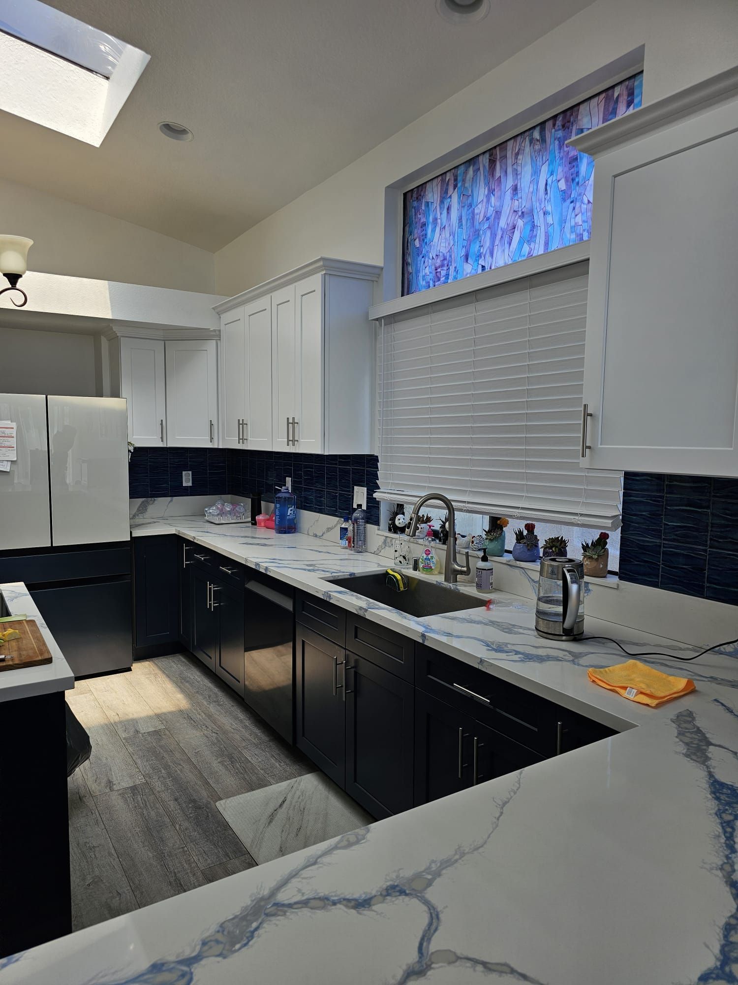 Bright modern kitchen with white cabinets, black lower cabinets, marble counters, and a window over the sink