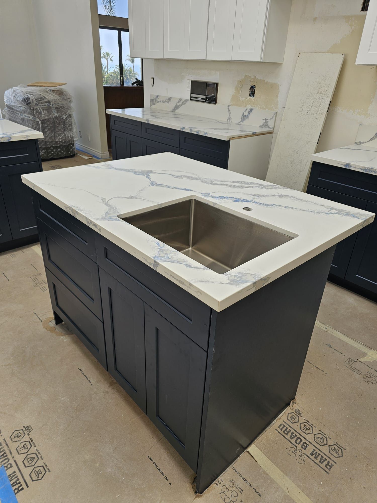 Kitchen island with dark cabinets and white countertop, featuring a stainless steel sink in an unfinished room