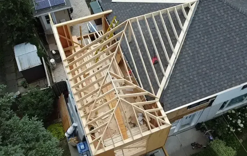 Aerial view of a house roof under construction with exposed wooden framing and dark shingles