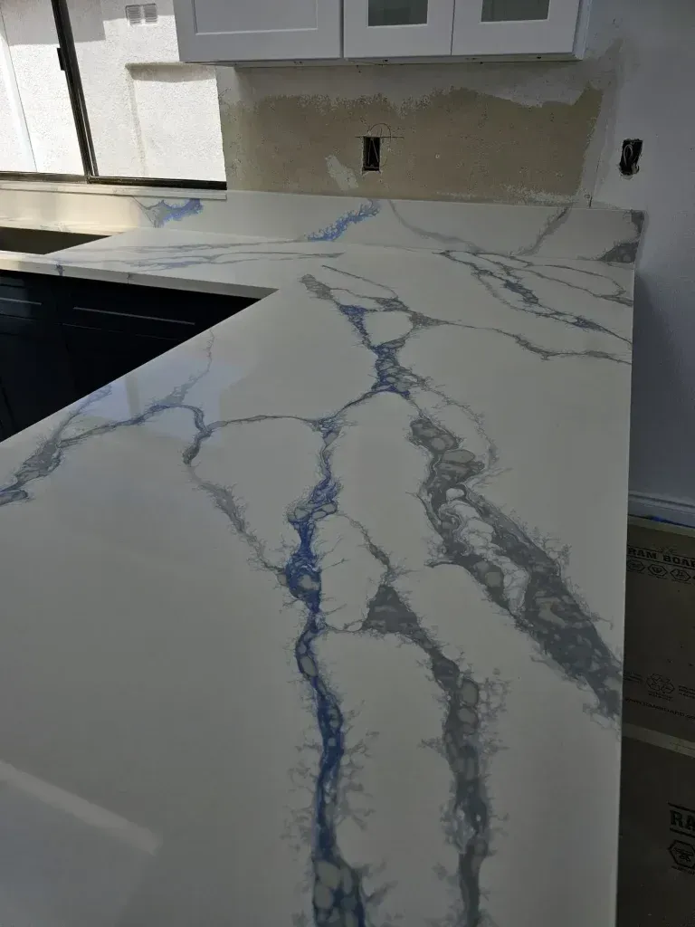 Kitchen countertop with white marble-look surface and blue-gray veining near a sink and cabinets