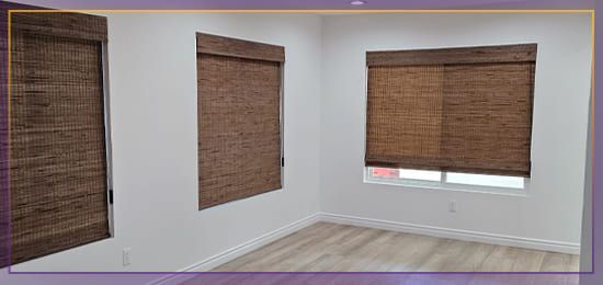 Empty room with three windows covered by brown woven blinds and light wood flooring