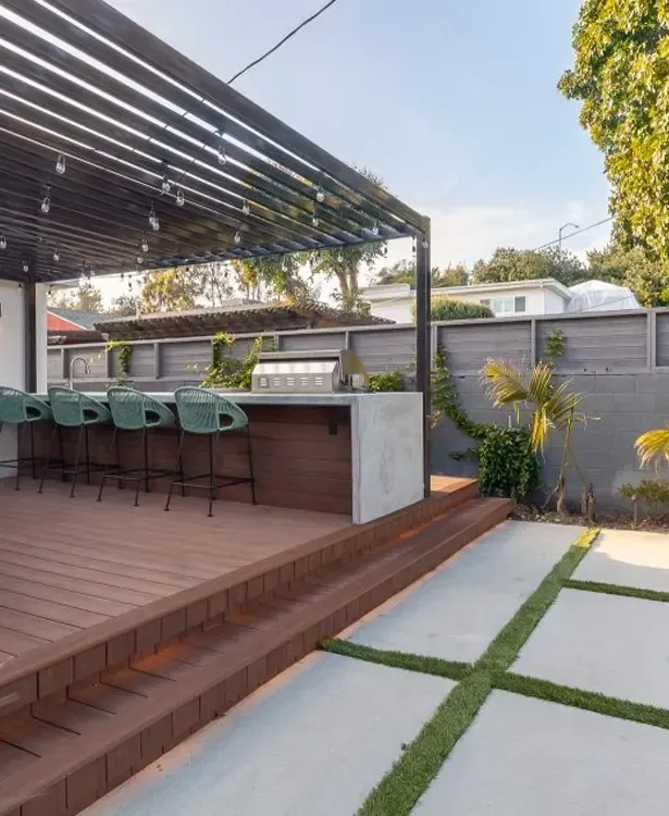 Modern backyard patio with bar seating, wooden deck, pergola, and stepping-stone path with grass.