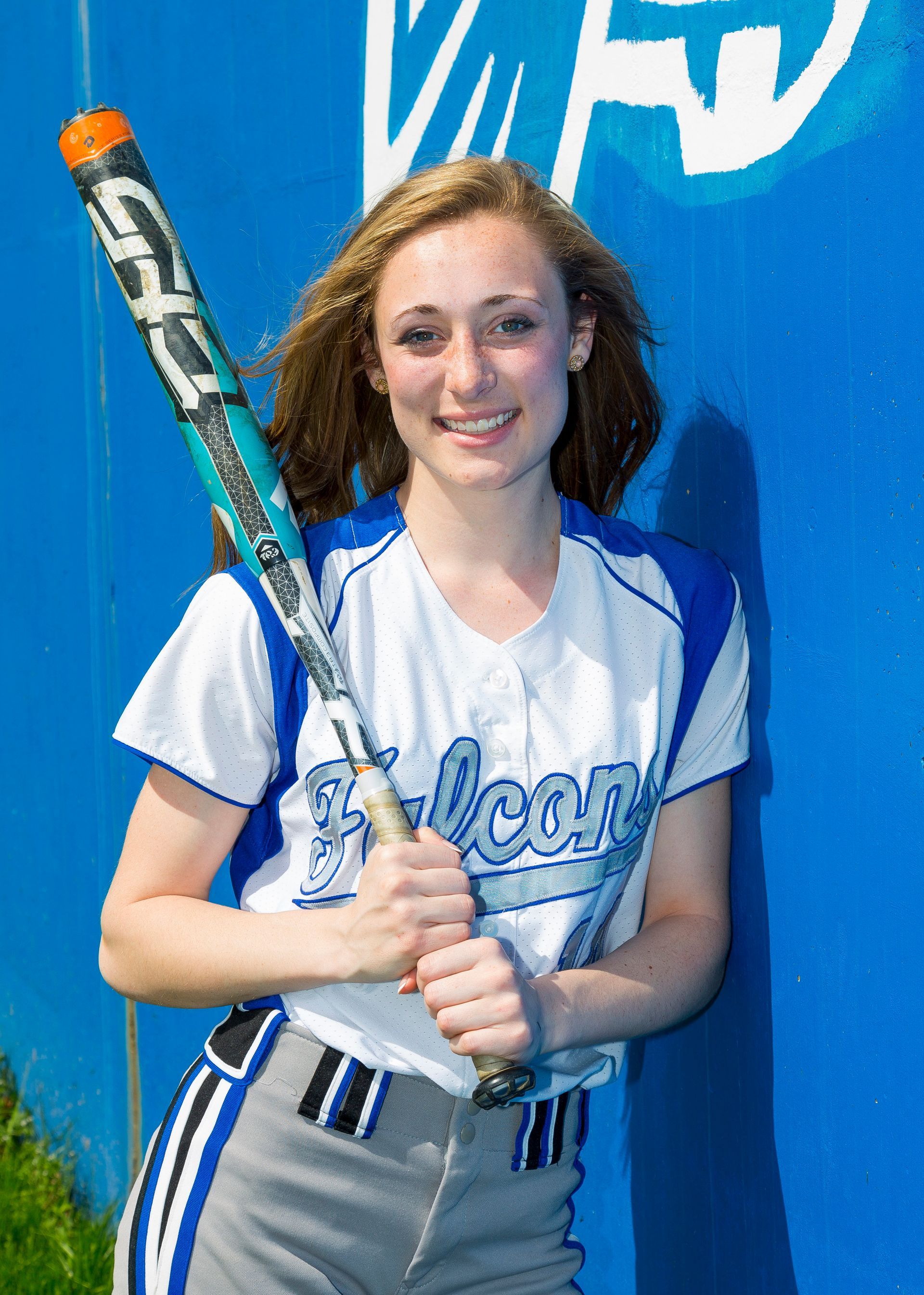 Woman in a blue jersey holding a baseball bat against a blue backdrop.