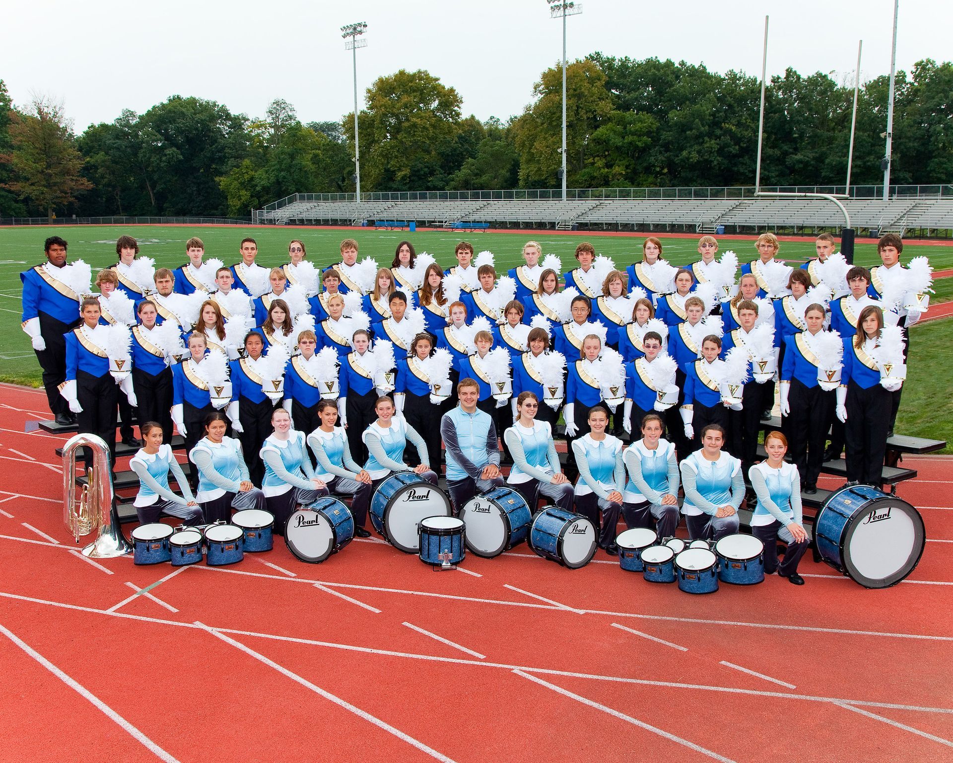 Large marching band in blue and white uniforms posing on a running track with drums in front