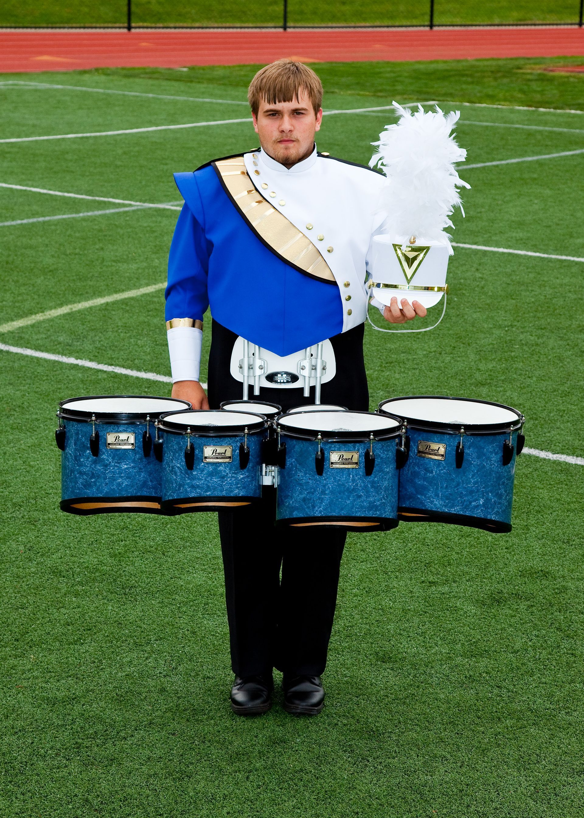 Marching band percussionist in blue and white uniform holding drumsticks on a football field