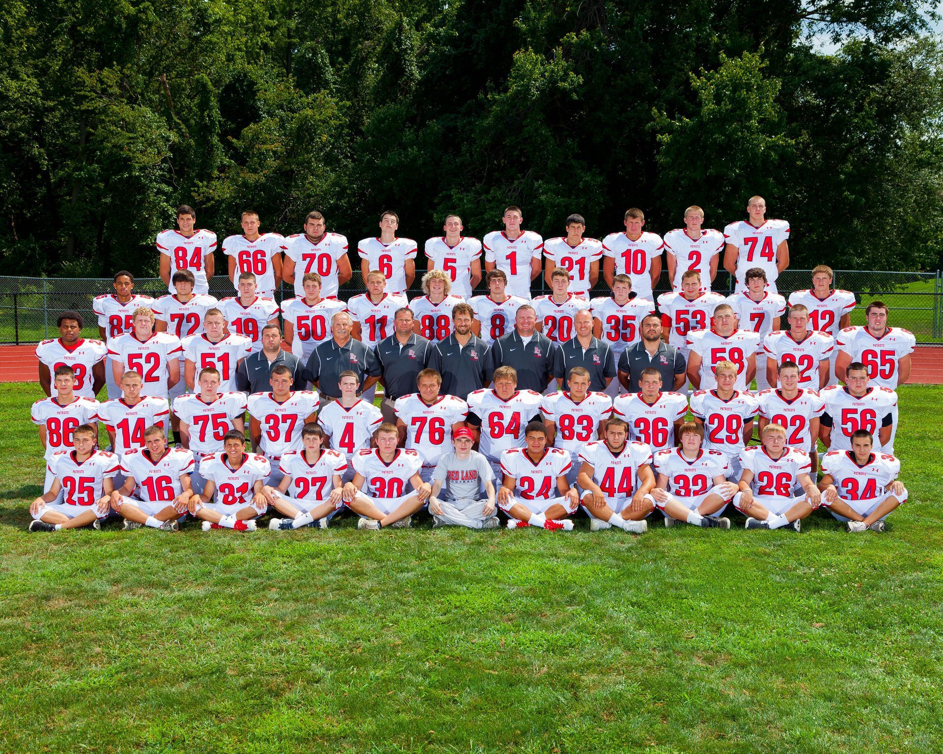 Large group of football players in white and red uniforms posing outdoors on a grassy field