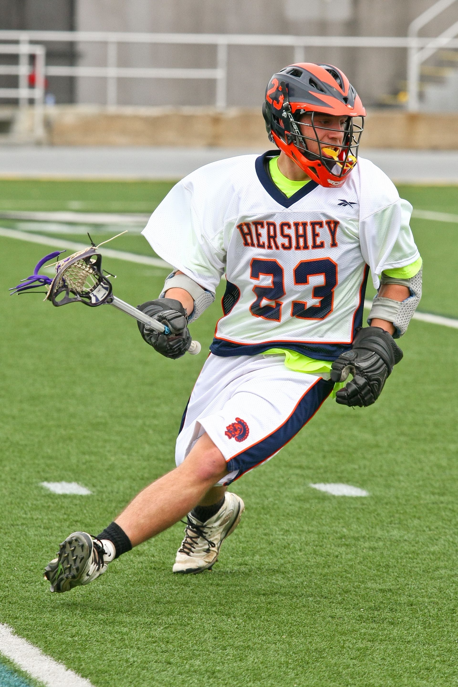 Lacrosse player in white and maroon jersey running on a field with a stick and ball