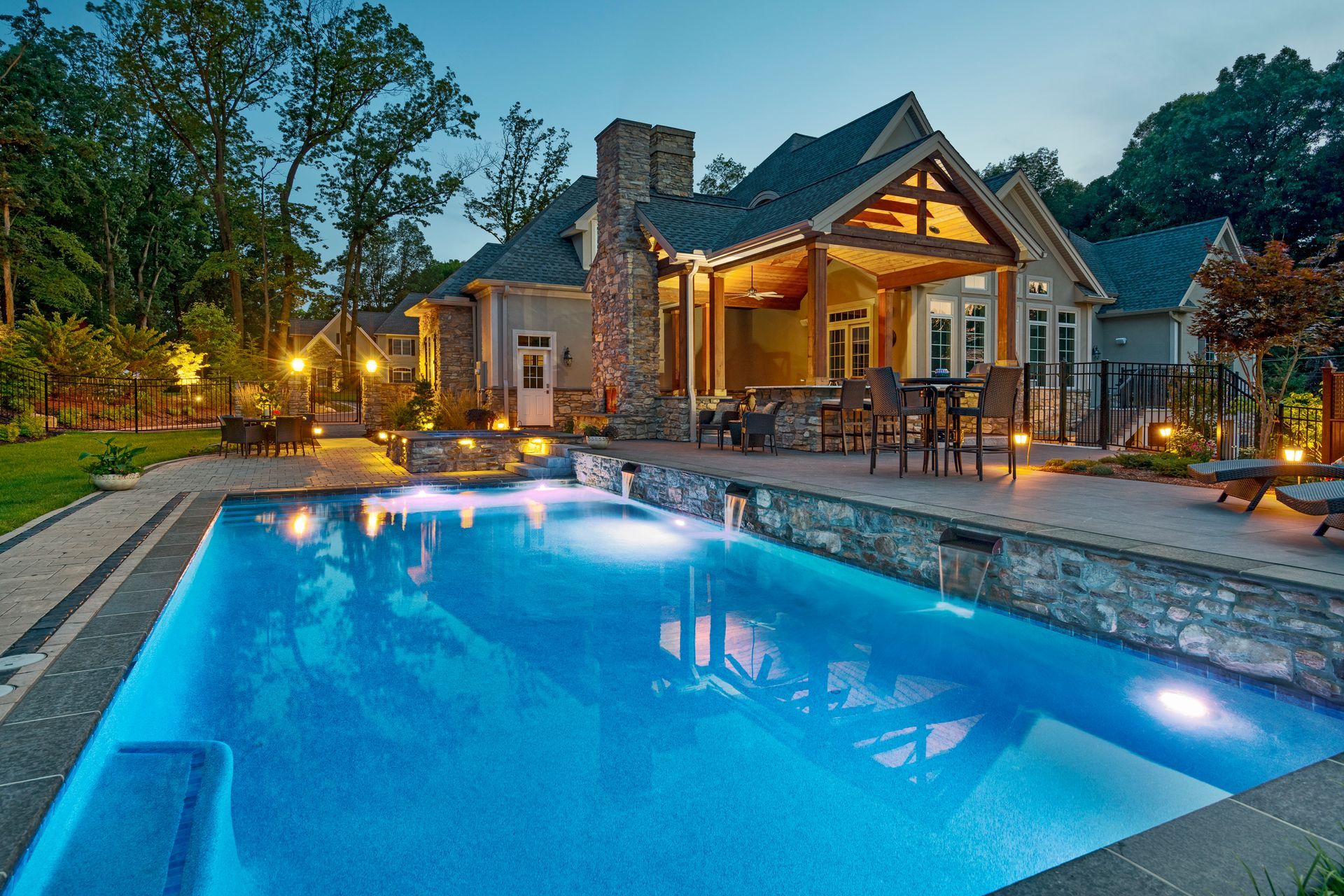 Luxury house with lit patio beside a glowing blue pool at dusk
