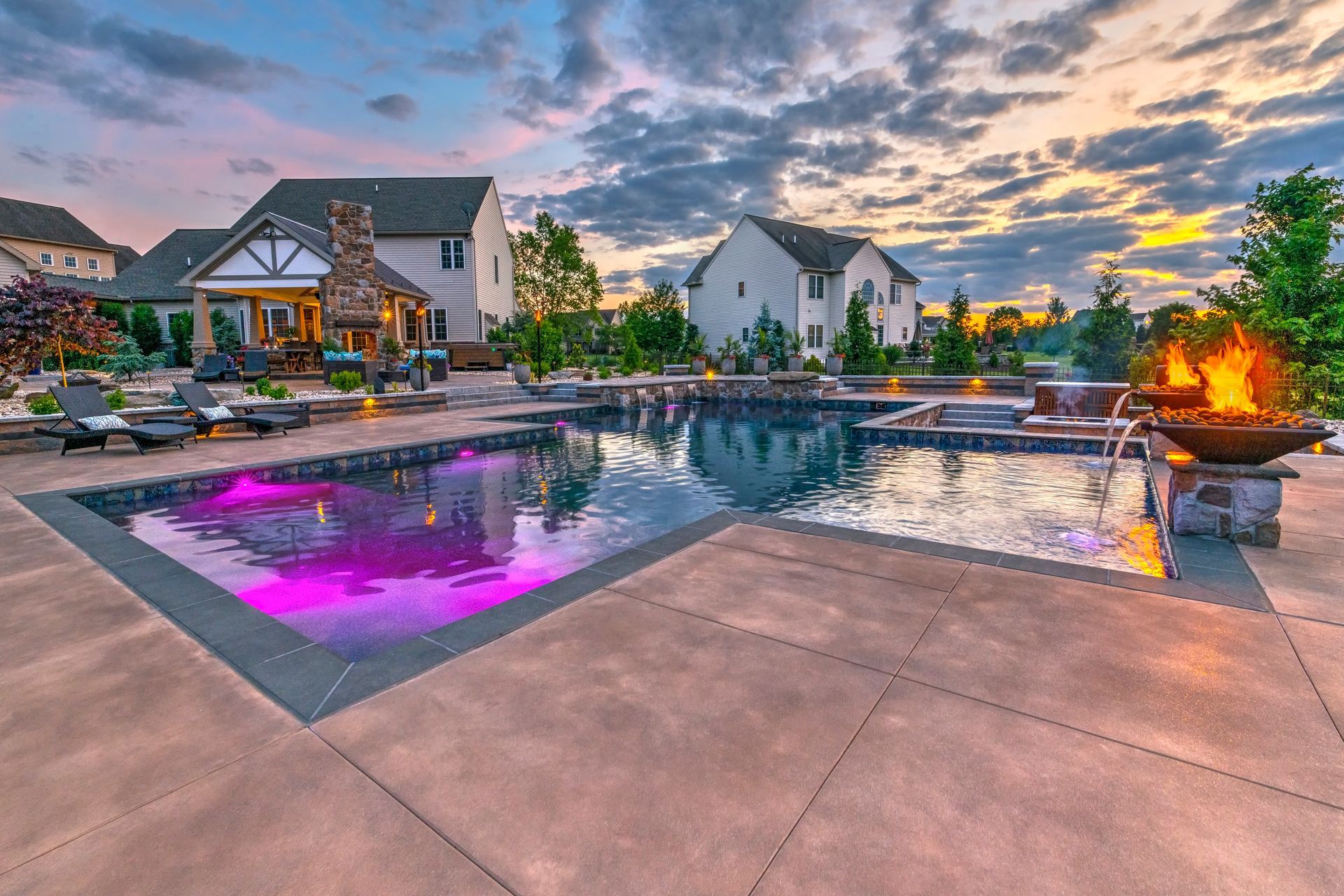 Modern apartment pool at sunset with purple-lit water, lounge chairs, and a fire pit