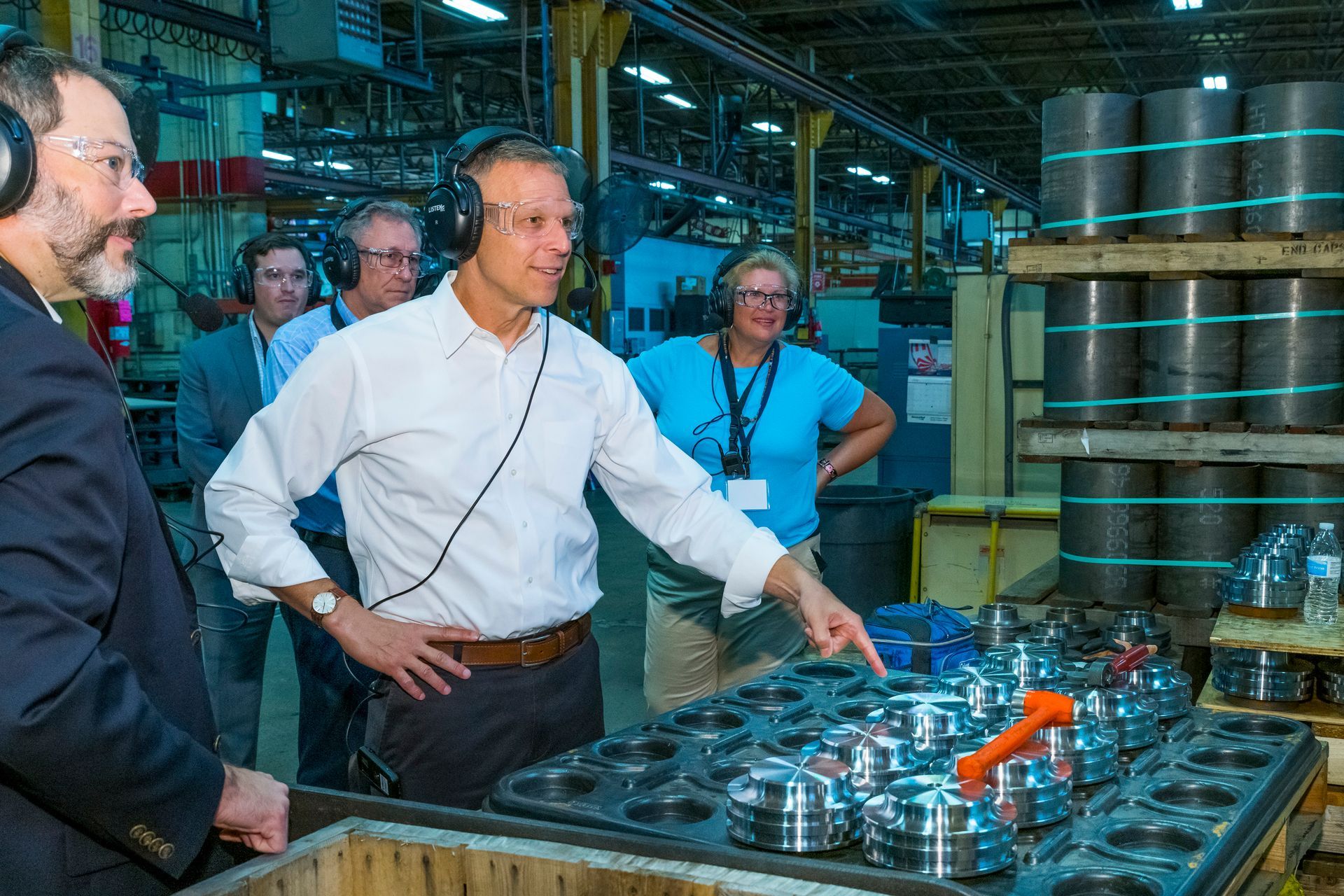 People touring a brewery, looking at metal kegs and equipment in an industrial warehouse