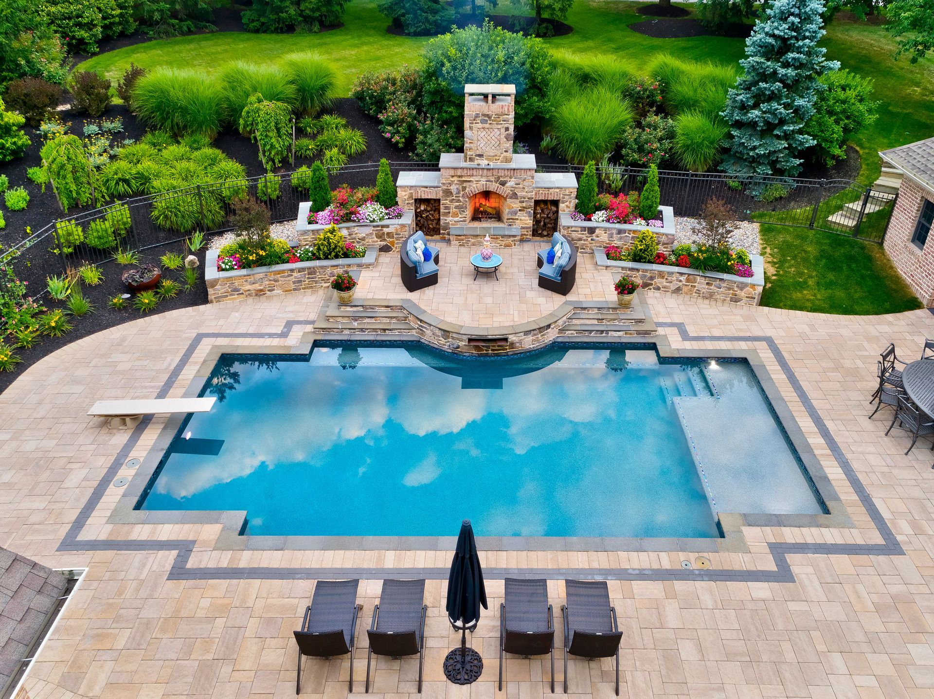 Backyard pool with stone patio, lounge chairs, umbrellas, and landscaped garden waterfall