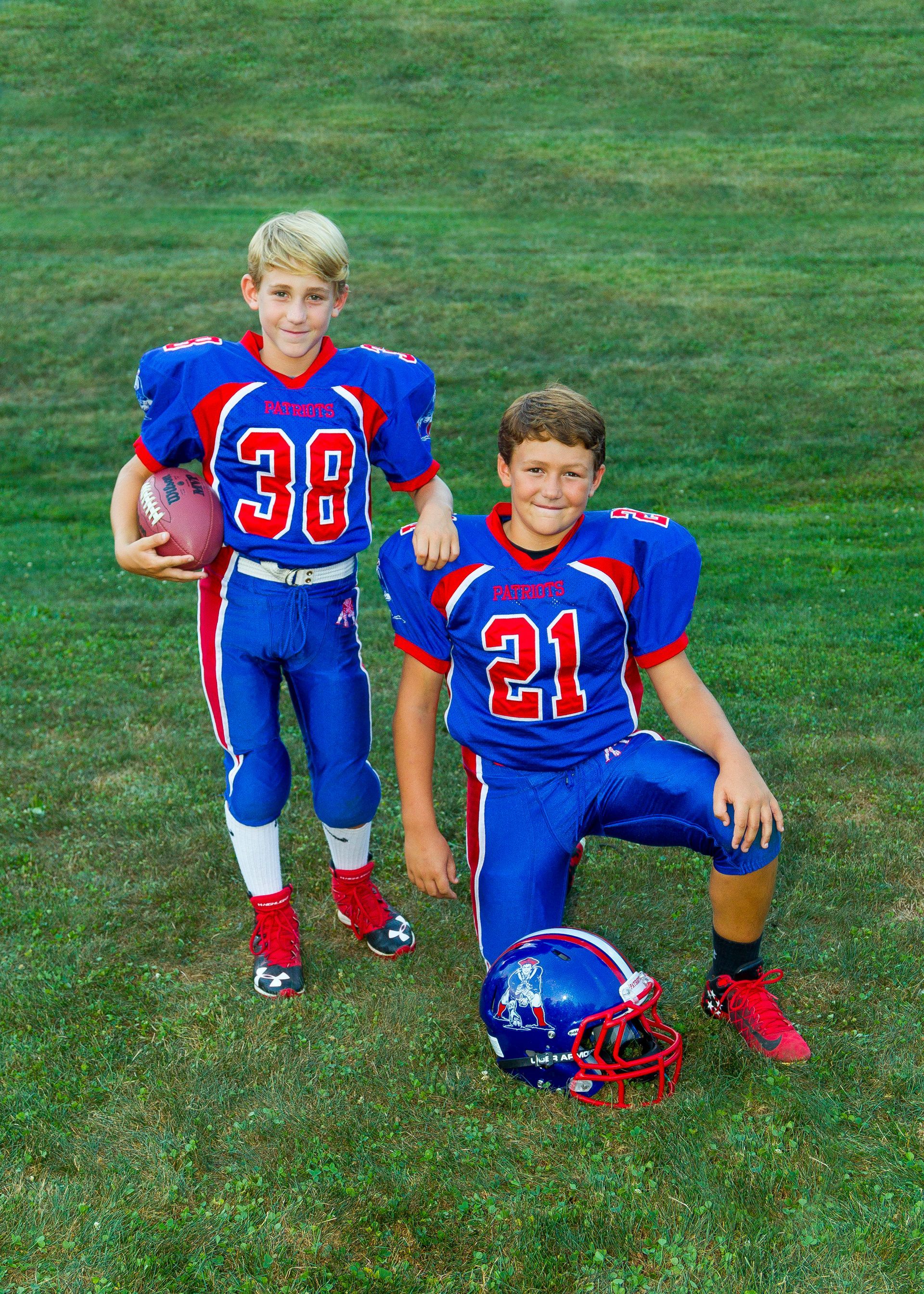Two football players in blue and red uniforms posing on grass with a helmet at their feet