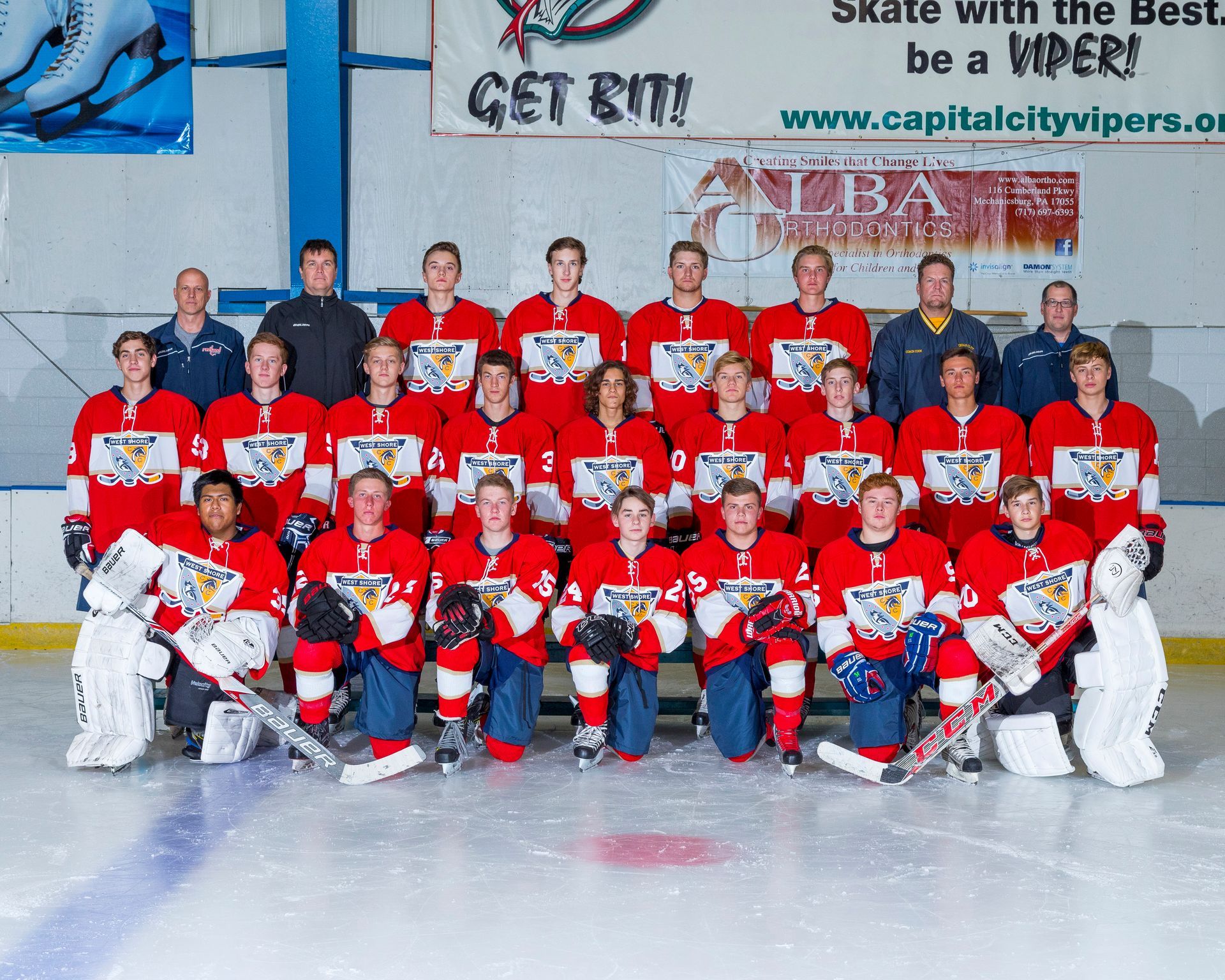 Youth hockey team in red jerseys posing on an ice rink with coaches and goalie equipment