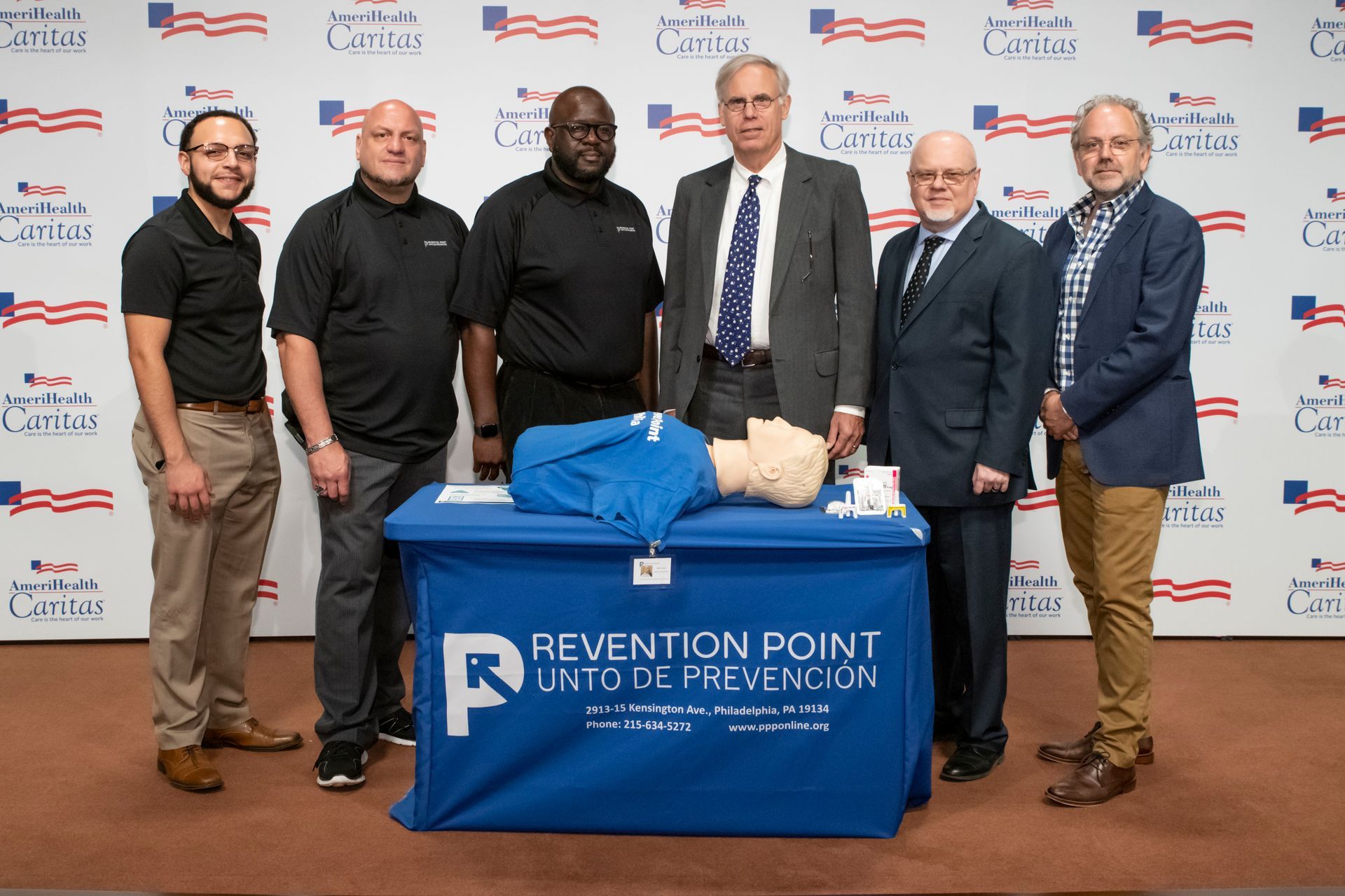 Six men pose behind a blue Prevention Point Philadelphia table at a formal event backdrop.