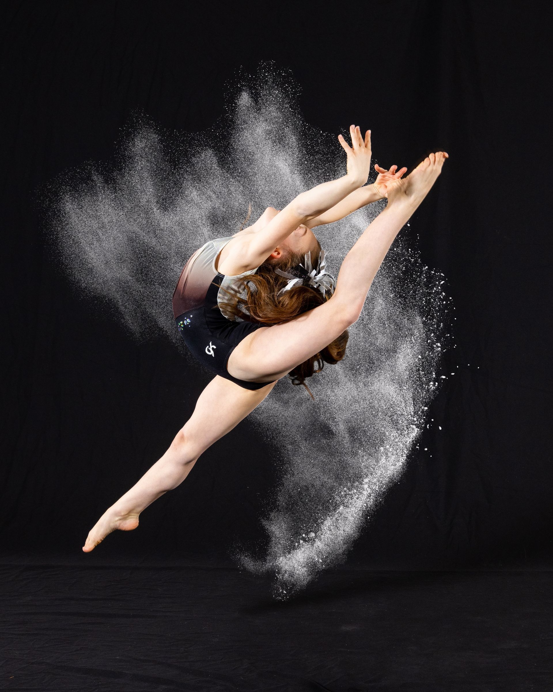 Dancer mid-air in a dramatic leap, surrounded by white powder against a black background