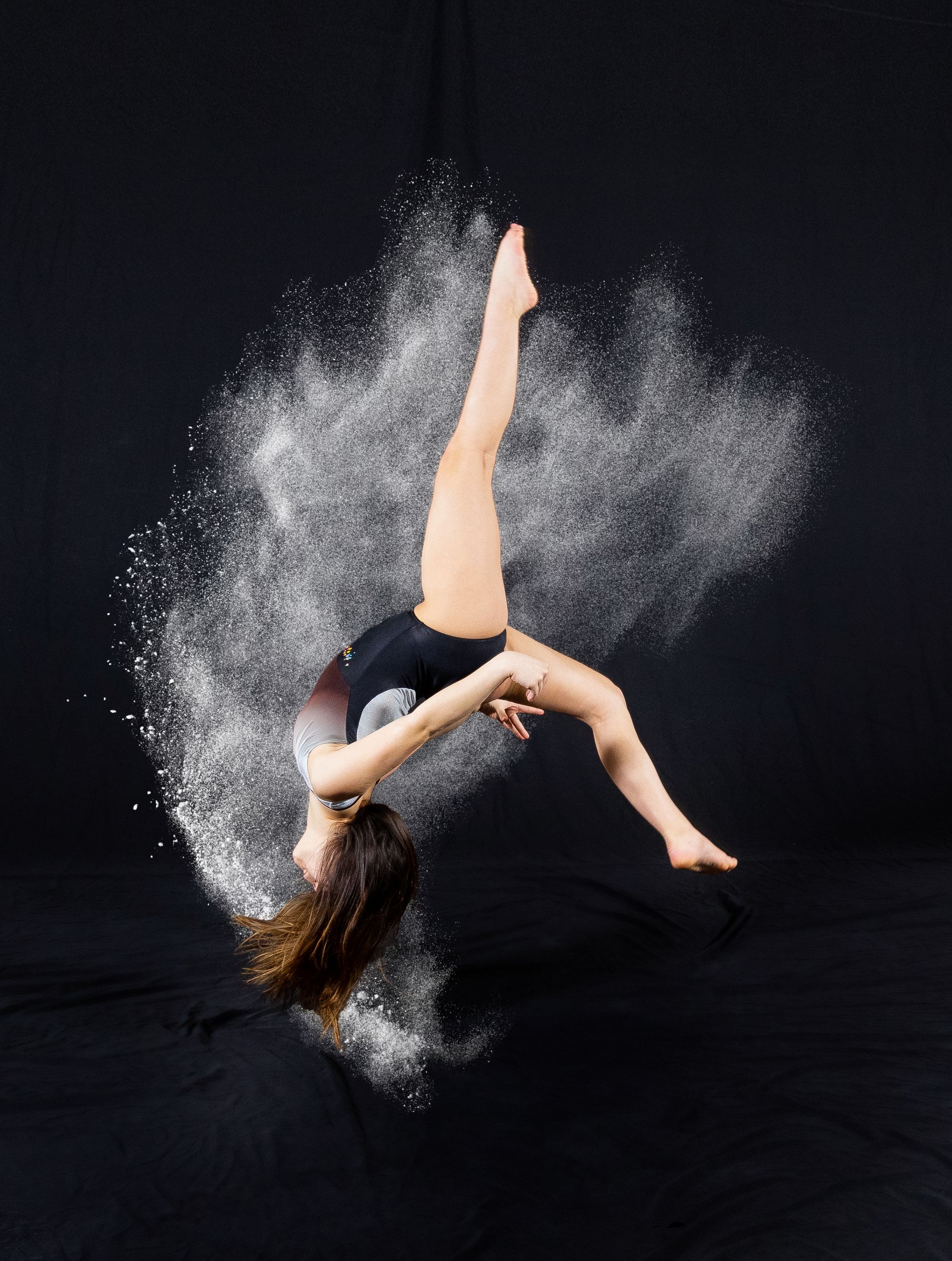 Contemporary dancer in a dramatic backbend, body arched amid a burst of white powder on a black background