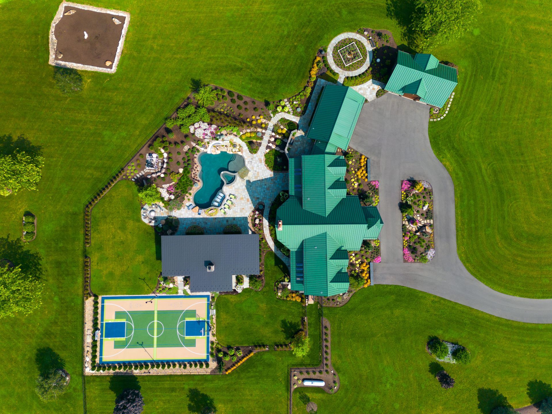 Aerial view of a large house with a pool, tennis court, driveway, and green lawn.