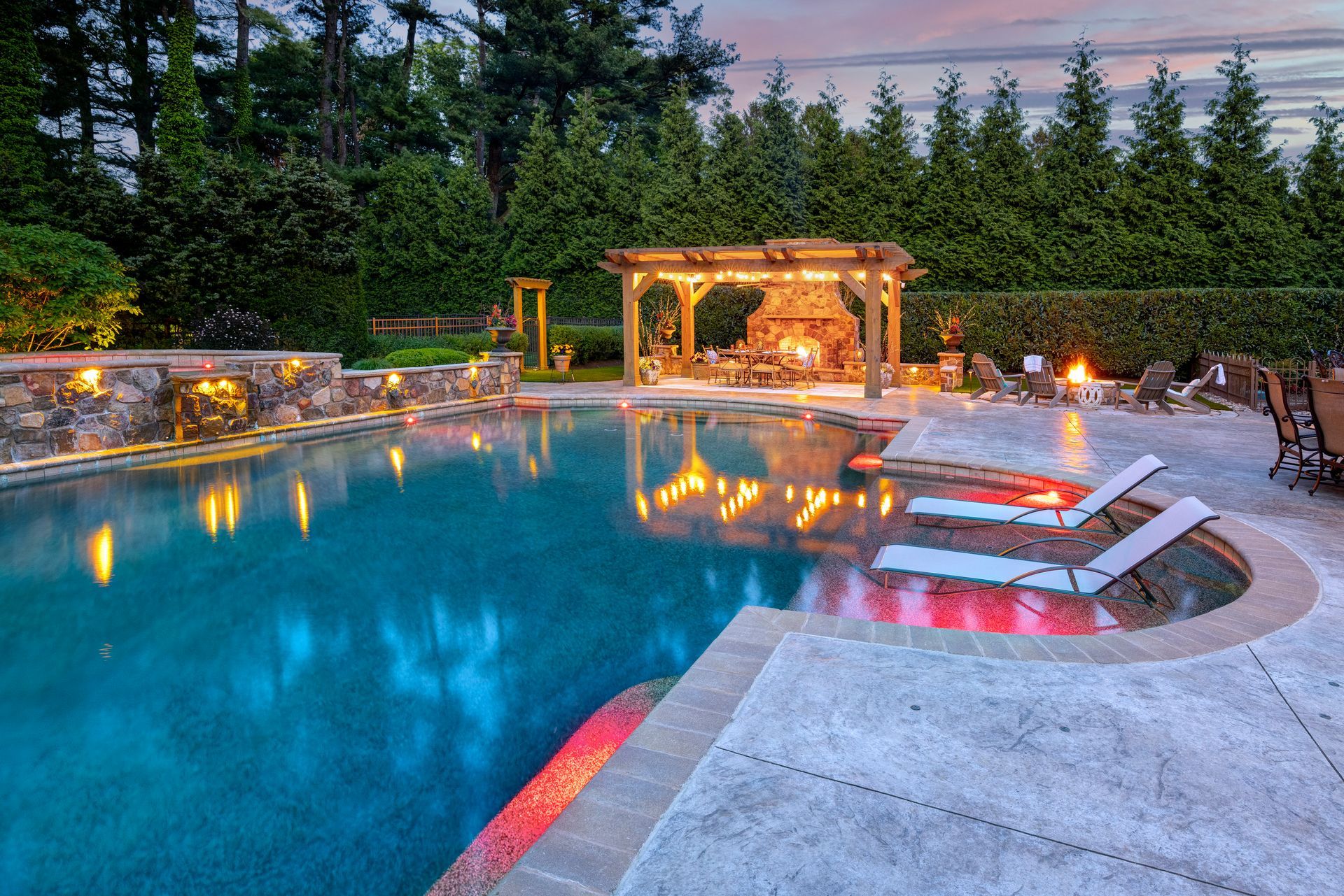 Luxury backyard pool with glowing waterfall spa, lit gazebo, and evening reflections