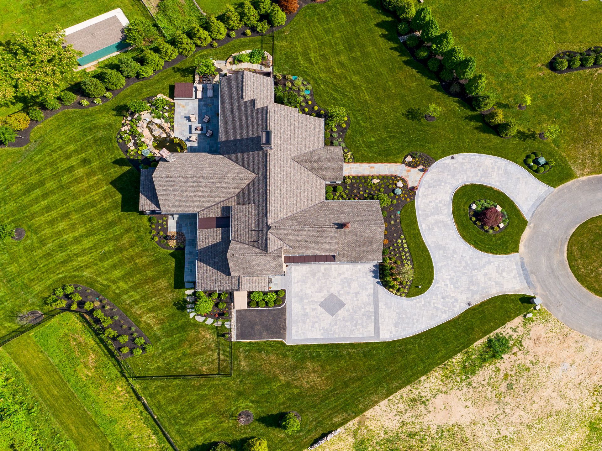Aerial view of a large house with a circular driveway, green lawn, and trees surrounding it