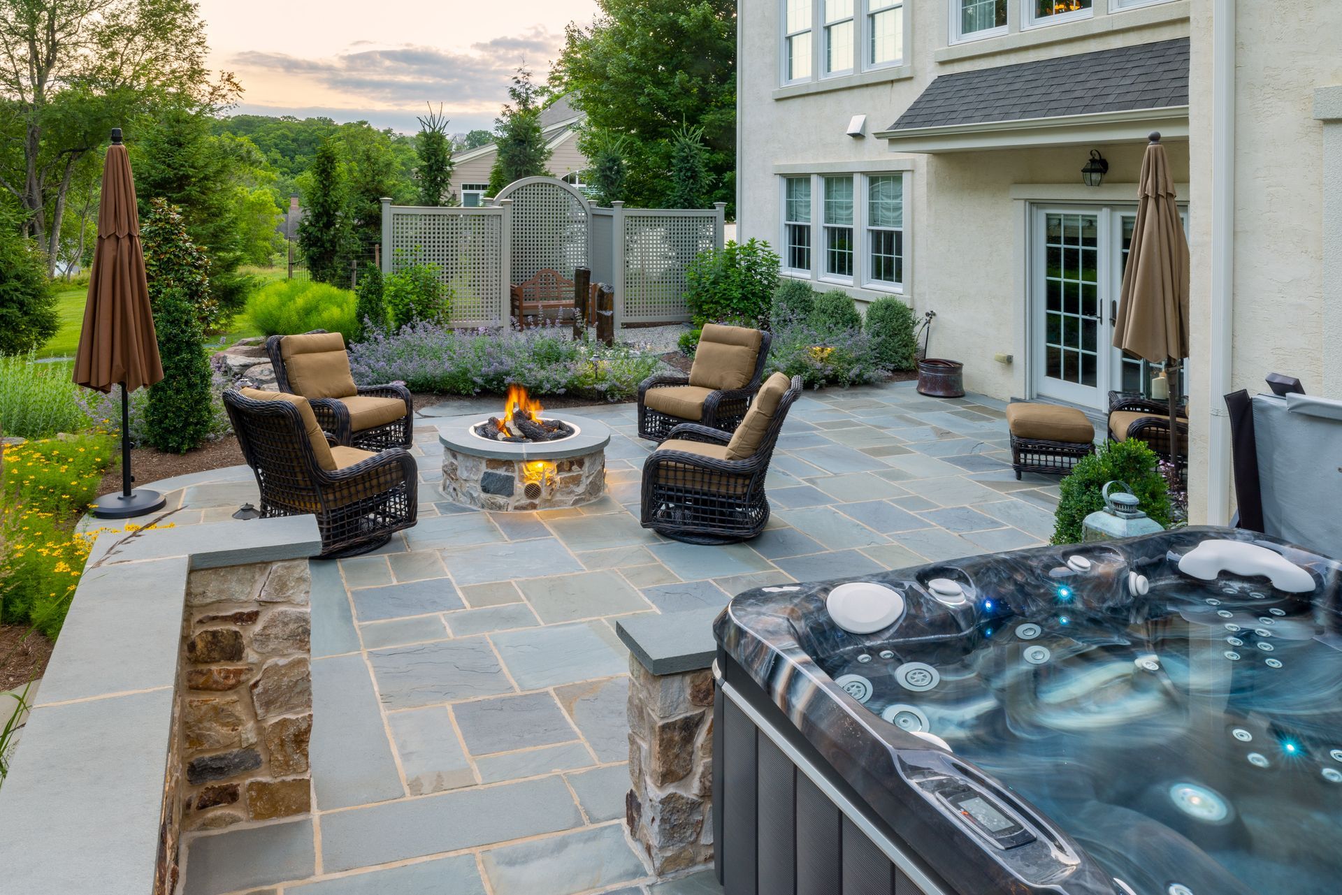 Backyard patio with fire pit, wicker chairs, hot tub, and a house at dusk
