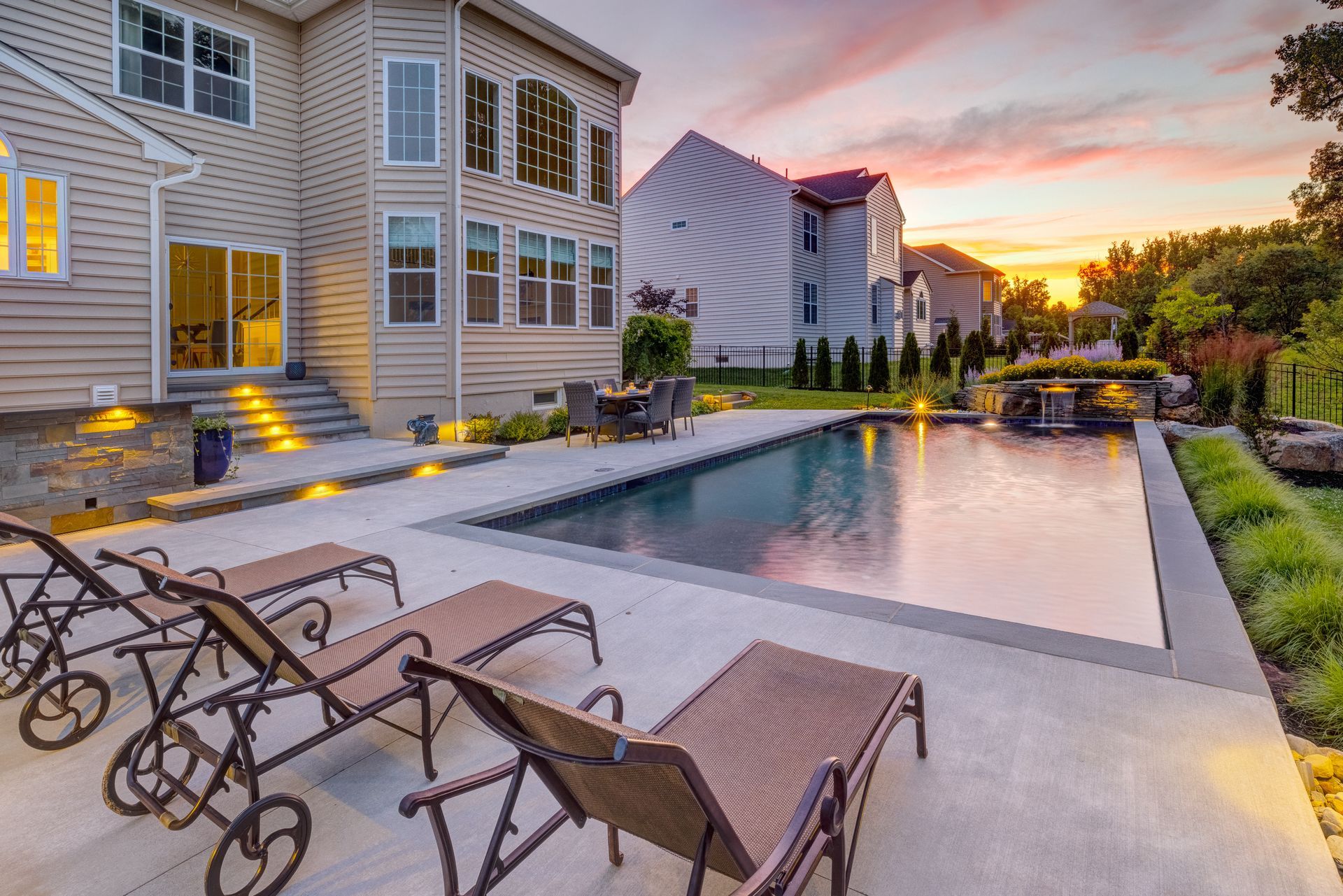Apartment pool and patio at sunset with lounge chairs and lit stairway