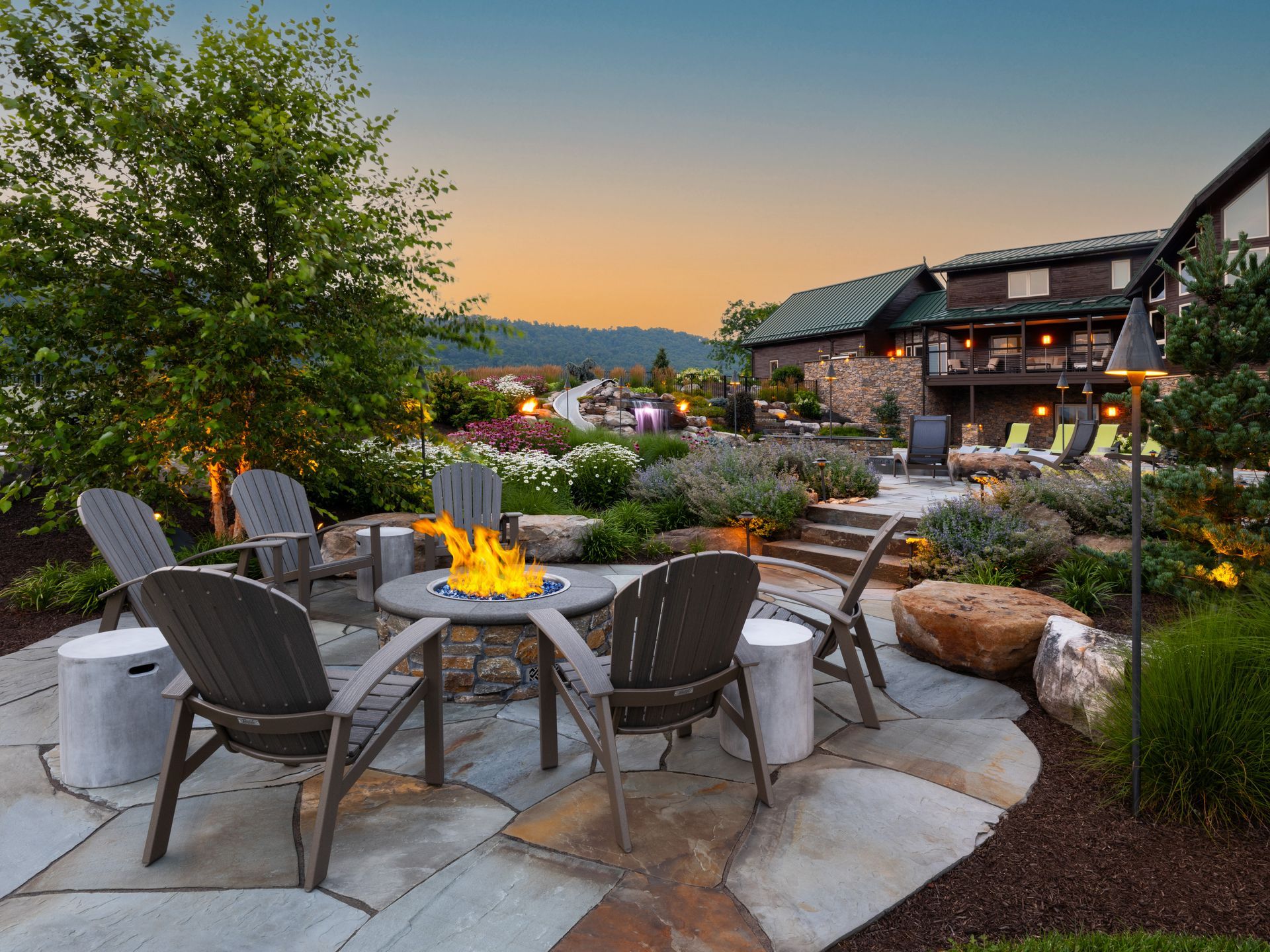 Backyard patio with fire pit, Adirondack chairs, and a house at sunset