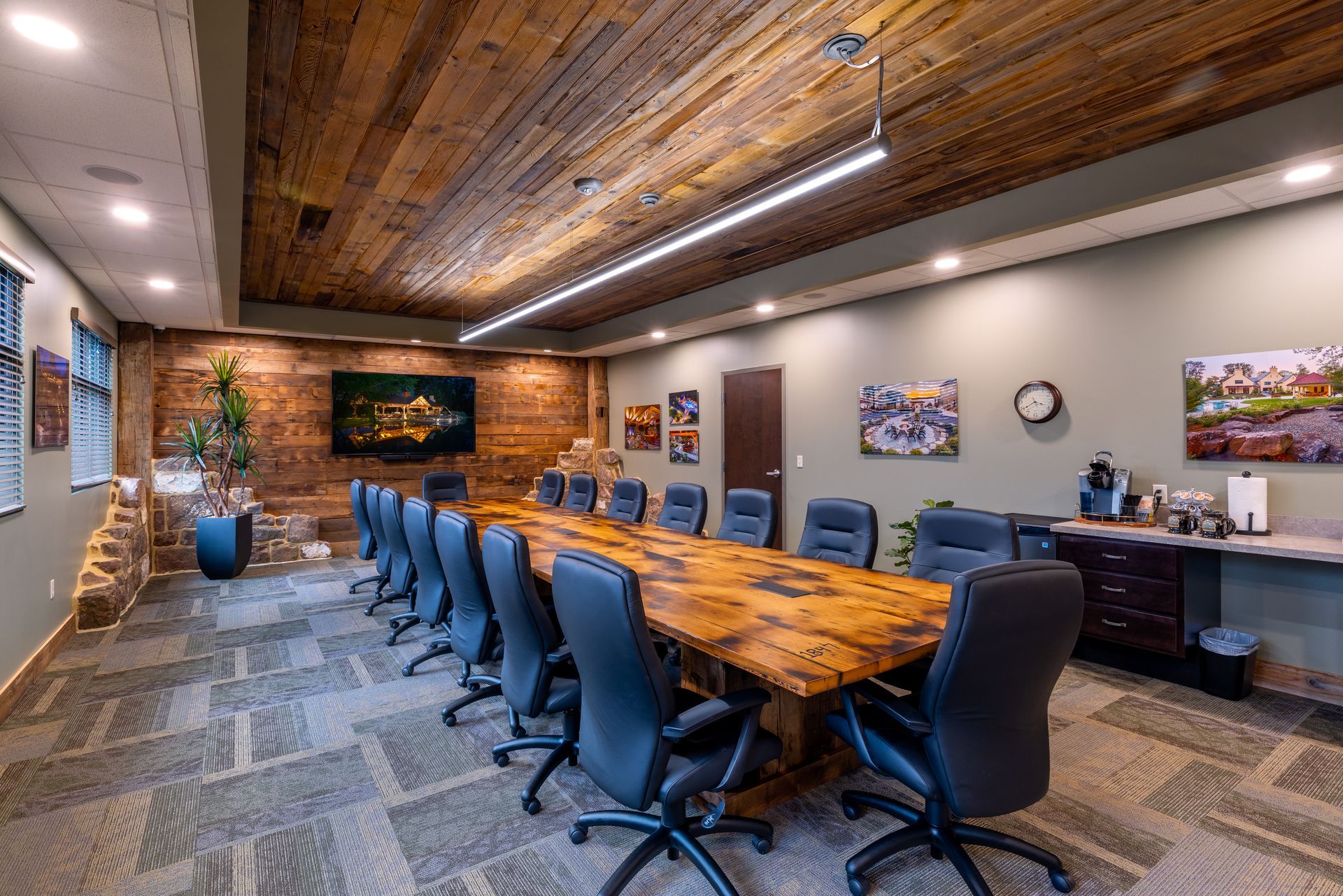 Conference room with long wooden table, blue office chairs, wood ceiling, brick wall, and wall art
