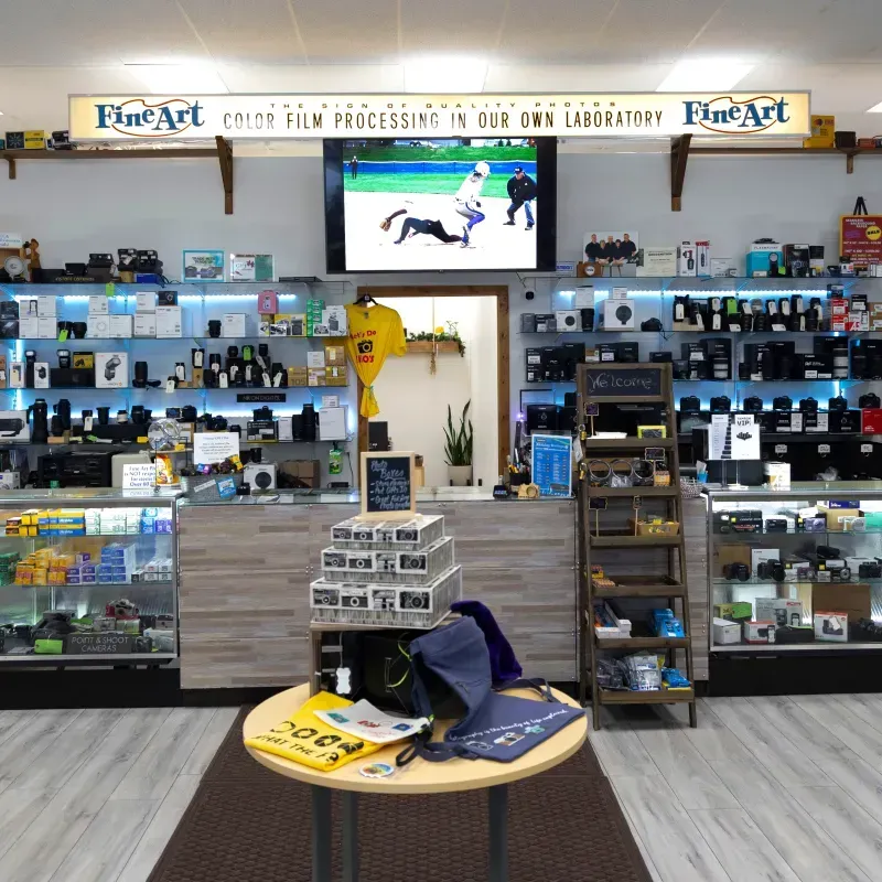 Camera store interior with shelves of equipment, a TV screen, and a round display table in front