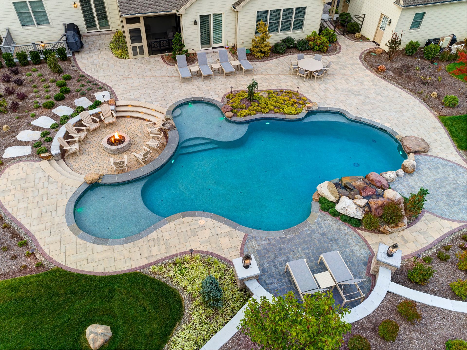 Backyard swimming pool with curved shape, lounge chairs, fire pit, and landscaped patio area