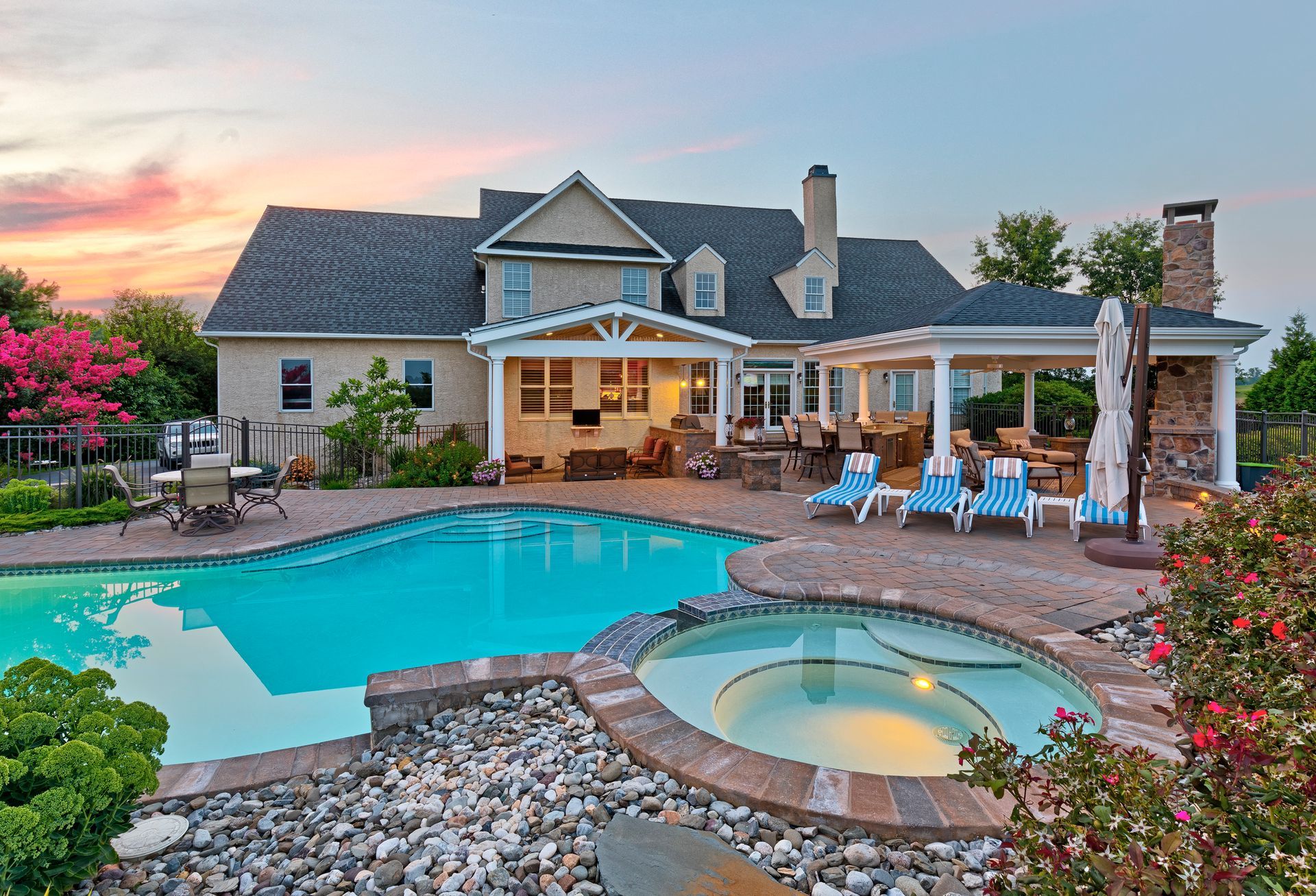 Luxury house with a turquoise pool and spa at sunset, featuring a patio seating area and landscaped yard