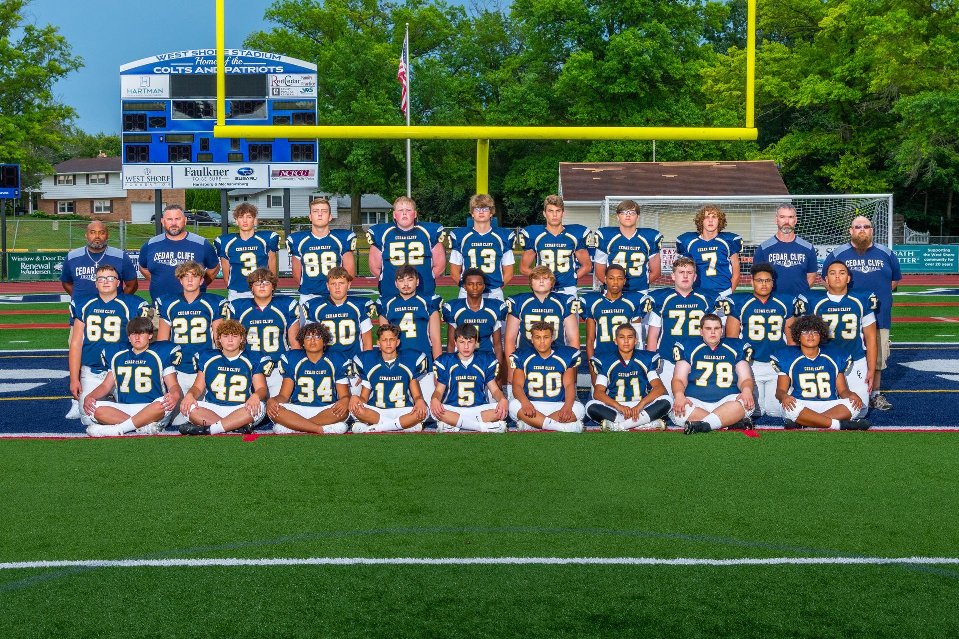 Youth football team posing on a field in blue jerseys with goalposts and bleachers behind them